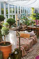 Greenhouse in garden, quilt and pillows on antique french iron bed, Myrtus in pots, brick floor 