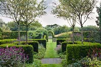 Archway with perennial borders and hedging. Monarda 'On Parade', Persicaria 'Firetail', Taxus baccata, hornbeam, Geranium.