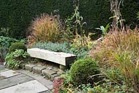 Curved wooden bench in Sybil's Garden surrounded by clipped yew, sedums and grasses showing autumn tints.