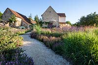 View of gravel path leading through naturalistic Dutch style planting towards house and terrace