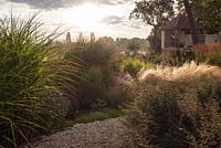 Gravel path leading through naturalistic Dutch style planting with Miscanthus, Nasella, perennials with pavilion in the background