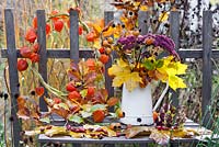 Autumn leaves and perennials in a jug - maple, Verbena, Rosehips, hornbeam, Sedum 'Herbstfreude', Verbena bonariensis. Physalis wreath.