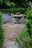 Taxus baccata hedge - Yew, rag stone patio with antique slate topped table and slatted chairs, and border of Nepeta 'Six Hills Giant' - Catmint 