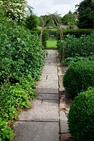 Stone pathway through fruit and vegetable garden with buxus balls - box and coppiced wood archway