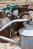 A collection of antique French copper and metal watering cans on a rusty iron table