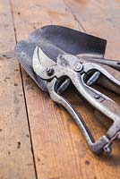 Vintage secateurs and hand trowels on a wooden surface