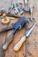 Collection of vintage garden tools on wooden surface. Widger, hand trowels, pot tamper, seed dibber, fork and secateurs