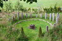 Wild meadow planted around circular firepit   with oak obelisks and Buxus pyramids.