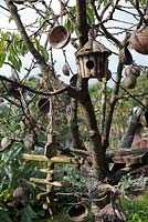 Plum tree living sculpture with hanging coconut shells, wooden mobiles and birdhouse.