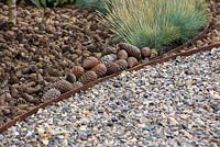 Border containing Festuca glauca 'Blaufuchs' and a mulch of pine cones, beside a path of knapped flint. Garden: The Flintknapper's Garden - A Story of Thetford. RHS Hampton Court Flower Show, July 2014