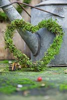 Christmas heart decorations made from moss, resting against a watering can. 