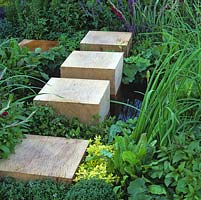 Wood oak cubes form stepping stones through planting and across small wildlife pool.
