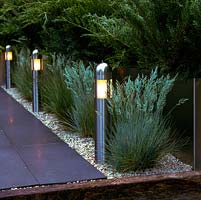Stainless steel lights illuminate pathway, set in gravel alongside clumps of Festuca glauca - blue fescue grass.