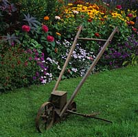 An old American Planet seeder rests on the grass by a summer bed of zinnia, verbena, helenium and gazania.