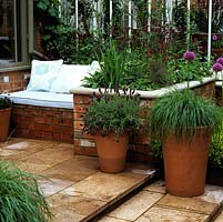 Raised flower bed doubles as side to brick seat with cushions, built in sunny position by conservatory.