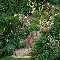 Spilling over a pebble path are lupins, hardy geranium, roses, lavender, verbena, campanula, daisy, dianthus and nicotiana, creating a riot of summer colour.
