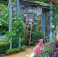 Adjacent to kitchen garden, an old stone garden shed, terracotta pots, rake, fork and hoe.