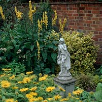 Stone statue stands in gold-themed courtyard, with plantings of verbascum spires, euonymus and daisy-like Inula hookeri.