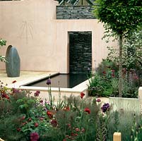 Modern courtyard with bronze resin seat and Lakeland slate wall reflected in still pool. Beds of cirsium, allium, rose, fennel, astrantia, salvia, euphorbia and hardy geranium. 
