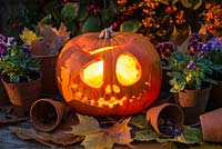 A pumpkin carved into a ghoulish face for halloween, a lighted candle inside.