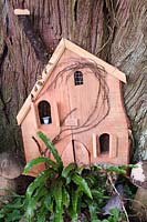 Child's miniature house at the base of a tree with ferns