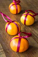Clementines wrapped with red ribbon for use as a festive hanging decoration