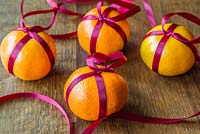 Clementines wrapped with red ribbon for use as a festive hanging decoration