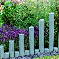 Sawn wooden poles of differing heights create edging to perennials. Poles painted to blend with silvery blue lavender.