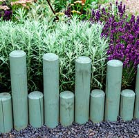 Sawn wooden poles of differing heights create edging to perennials. Poles painted to blend with silvery blue lavender and artemisia.