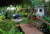 Wooden footbridge decorated with red Pelargoniums with white garden shed in urban backyard garden in summer, Quebec, Canada