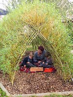 Brothers Jacob and Loui with their mother, Ali Rose, play on the floor in the shade of a tunnel  woven from living Salix viminalis - willow.