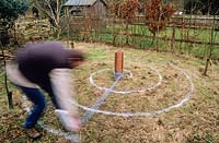Man tracing spiral on rough grass in autumn with can of marker paint in order to plant a crocus spiral feature for spring