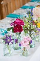 Roses and clematis in a cutflower arrangement, with a group of bottles as vases, for a wedding