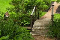 Cedar mulch path and old wooden footbridge with birdhouse in border in front yard country garden in summer, Quebec, Canada