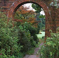Brick arch frames view of path leading to main lawn, overhung by Parrotia persica, its leaves turning red and gold for autumn.