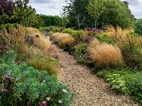 A gravel path lined by double mixed borders planted with perennials and grasses. Planting includes Euphorbia, Achillea, Sedum, Eupatorium, Monarda, Guara and Rudbeckia with Stipa and Calamagrostis grasses.