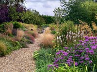 A gravel path lined by double mixed borders planted with perennials and grasses. Planting includes Veronicastrum, Achillea, Sedum, Eupatorium, Monarda, Guara and Geranium with Stipa and Calamagrostis grasses.