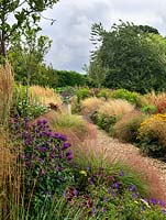 A gravel path lined by double mixed borders planted with perennials and grasses. Planting includes Echinacea, Achillea, Sedum, Eupatorium, Monarda, Guara and Rudbeckia with Stipa and Calamagrostis grasses.