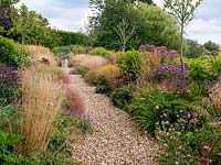 A gravel path lined by double mixed borders planted with perennials and grasses. Planting includes Echinacea, Achillea, Sedum, Eupatorium, Monarda, Guara and Rudbeckia with Stipa and Calamagrostis grasses.