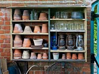 Shelves built from reclaimed timber offcuts house terracotta plant pots, glass jars and lanterns, making use of a wall for storage in this tiny town garden.