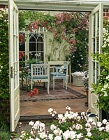 Seen from rose filled courtyard, conservatory with pink and white bougainvillea trained up the wall above seating area