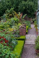 Pathway through the walled Exotic Garden at Abbeywood featuring box edged borders planted with Dahlia, Ricinus, banana, Verbena bonariensis, Olea europea and Trachycarpus fortunei palms.