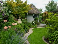A shaped grass path leads through mature mixed borders to a thatched summer house.