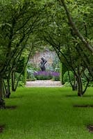 An avenue of Malus toringo var. sargentii trees leading to a contemporary sculpture in a walled garden.