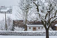 Winter scene with hedge and the northern face of a wooden house