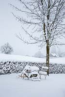 Garden furniture buried under snow, in the background, a hedge and winter landscape