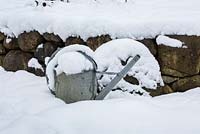 Snow on tin watering can and dry stone wall
