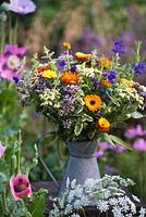 Galvanised jug filled with arrangement of herbal plants - feverfew, marigold, clary sage, oregano, mint, rosemary, lavender.
