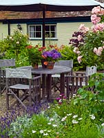 Table and chairs with pots of geranium and hydrangea. Beds of lavender, roses and cosmos.
