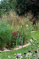 A curved grass path alongside a mixed herbaceous border planted with Monarda, Dahlia, Calamagrostis, Stipa and Molina.